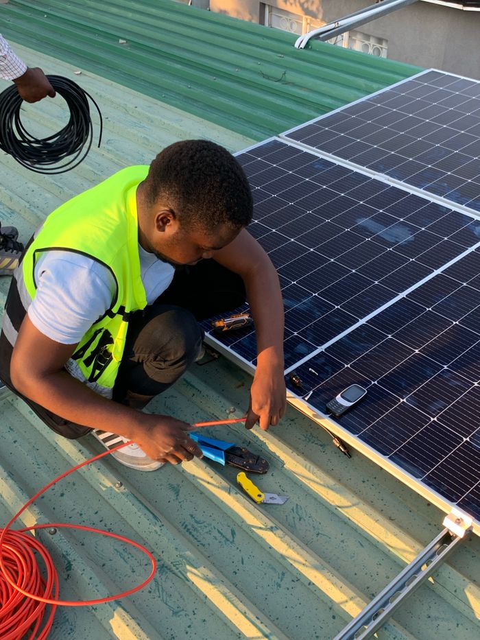 footer-cta Technician working on solar panel installation with cables and tools on a sunny day.