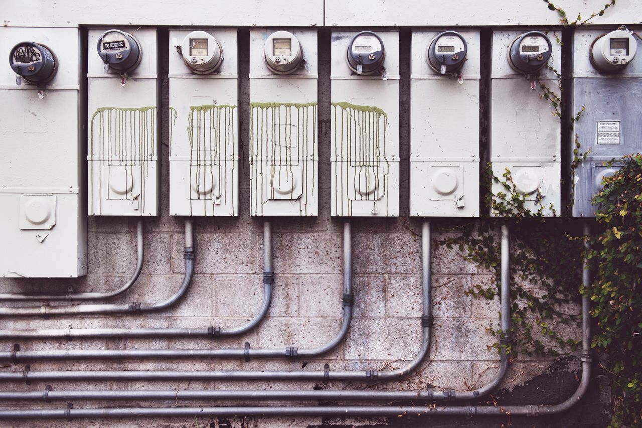 services-03 Array of outdoor electric meters on a brick wall with vines.