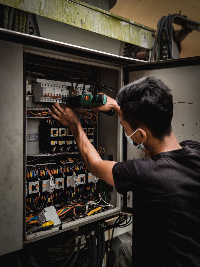 services-05 Technician working on circuit breaker panel, adjusting electrical wires indoors.